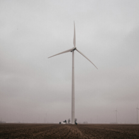 A wind turbine shrouded in fog in the middle of a brown field with more turbines in the distance