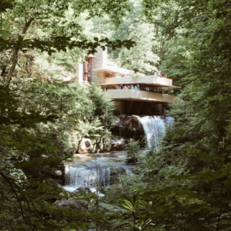 Brown futuristic home with waterfalls beneath it surrounded by a lush, green forest