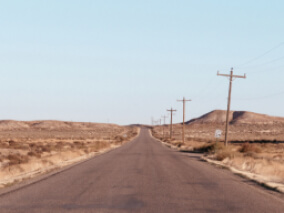 A highway stretching out into the distance in a desert landscape with telephone lines on the right side