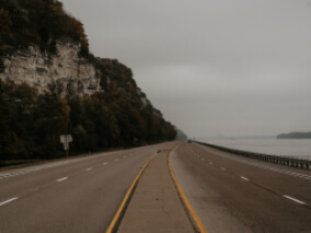 An empty freeway with a rocky hillside on the left side and water on the right side