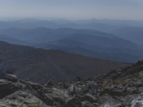 View from the top of a rocky hillside with brown/grey hills rolling into the distance